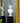 Two white classical-style female bust sculptures displayed on black pedestals in front of a blue wallpapered wall with gold floral motifs and mustard yellow curtains.